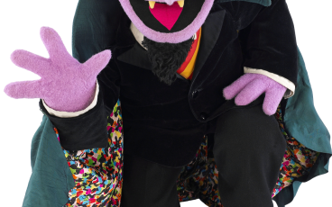 count von count from sesame street kneeling and showing all four fingers on his right hand, possibly having just counted to four or just waving hello