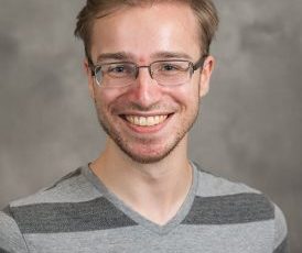 Picture of a man wearing glasses wearing a striped gray shirt with a gray background.